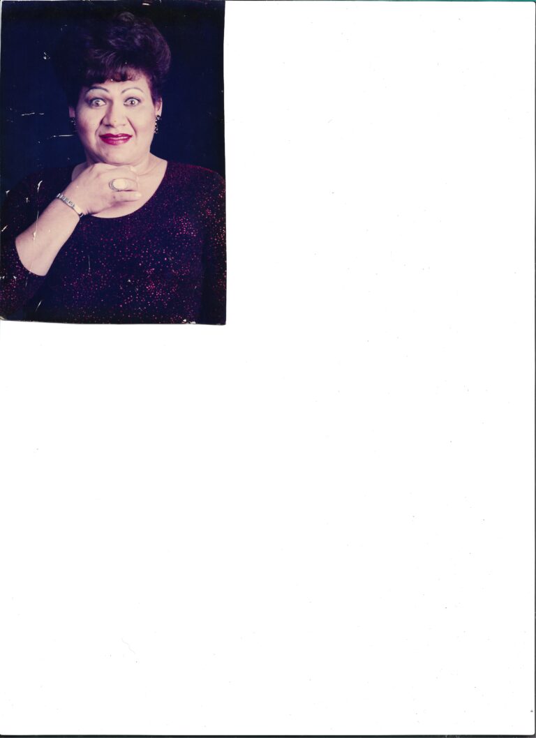 Digitalização de foto, em um dos cantos de uma folha A4. A foto está com algumas falhas em branco, mas nada que impeça a visualização da figura como um todo. A pessoa na foto é Keila Simpson, está usando batom vermelho, pulseira e anéis, está com os olhos bem abertos e tem a mão no queixo.