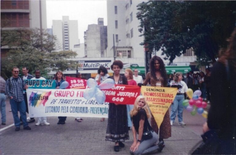 Digitalização de foto analógica do encerramento do V ENTLAIDS. Não há marcas. Na foto, é possível ver várias pessoas segurando faixas e bandeiras pedindo justiça e cidadania para homossexuais e travestis.